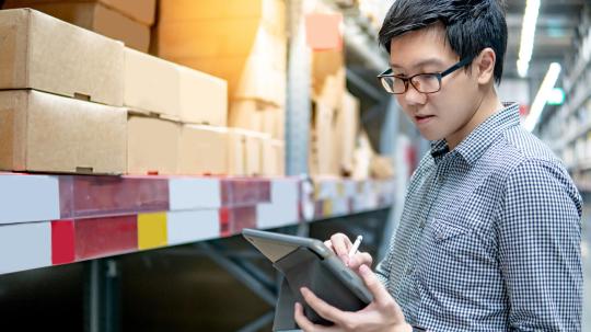 Asian man doing stocktaking on tablet in warehouse