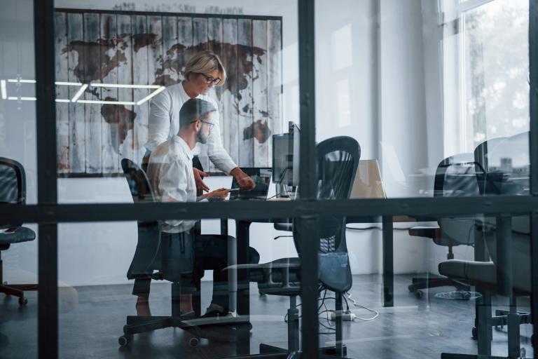 View through the glass. Two stockbrokers in formal clothes works in the office with financial market